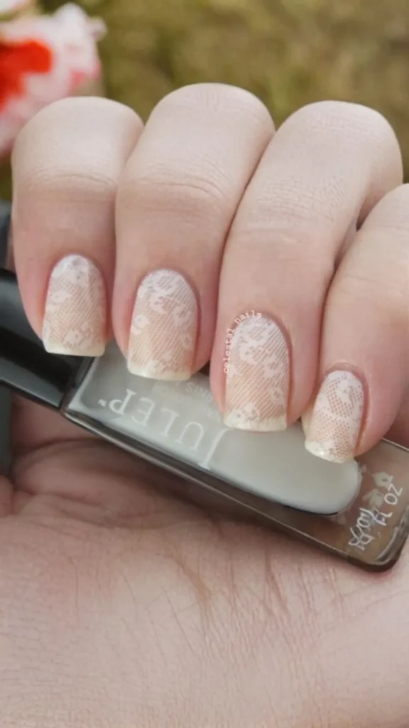 Close-up of a person's hand holding a white bottle of Julep nail polish, showcasing a manicured set of square-shaped nails. The design features an intricate white lace pattern stamped over a sheer, pale ivory base coat. A faint "celestial nails" watermark is visible near the cuticle of the ring finger.
