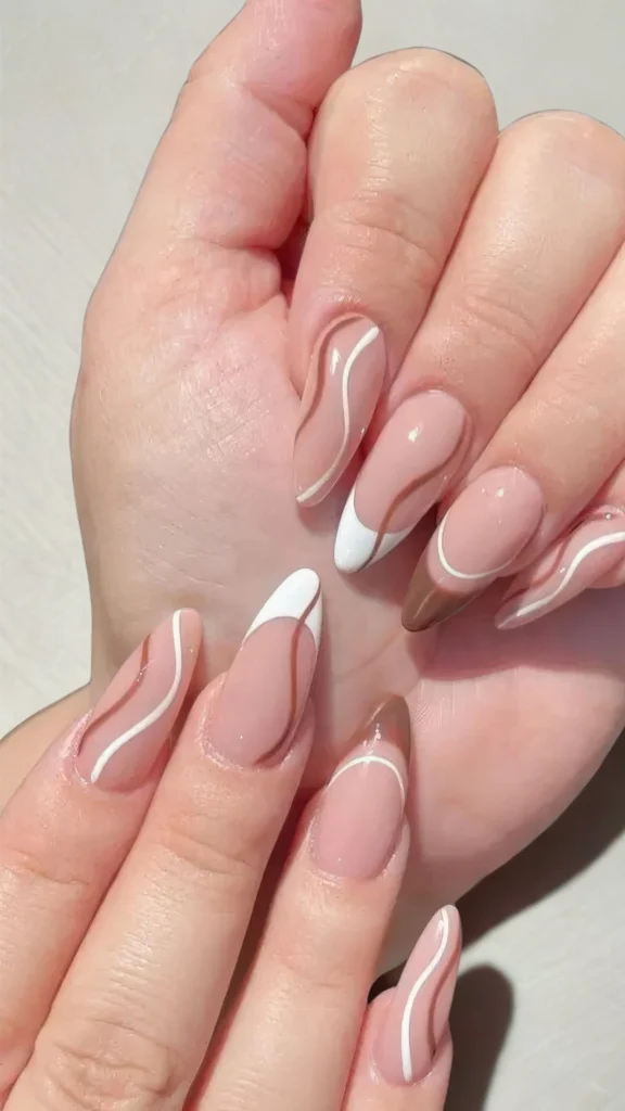 Close-up of hands displaying a retro-inspired abstract manicure on long, almond-shaped nails. The design features a glossy nude base decorated with flowing, organic swirl lines in crisp white and warm chocolate brown, with some nails integrating a classic white French tip accent.