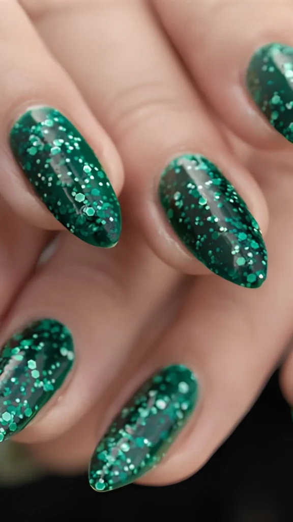 Close-up of a hand displaying a glittering green nail art manicure on long, oval almond-shaped nails in the file 5_3.webp. The design features a deep, glossy forest green jelly or creme base heavily layered with sparkling green and silver micro-glitter and larger hexagonal glitter flakes, creating a multidimensional, starry night sky effect across each nail.