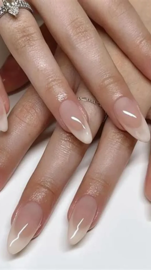 Close-up of a person's hand showcasing an elegant, modern French manicure on almond-shaped nails. The body of the nails features a smooth, velvet-like matte nude pink finish, while the very tips are finished with a starkly contrasting ultra-glossy clear top coat.