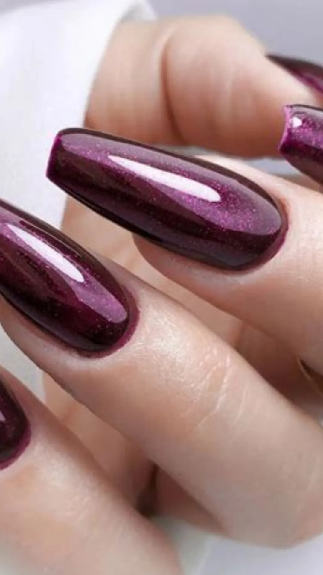 Close-up of a glamorous winter manicure featuring long coffin-shaped nails painted in a rich, shimmering burgundy cat-eye polish with a velvet-like finish.