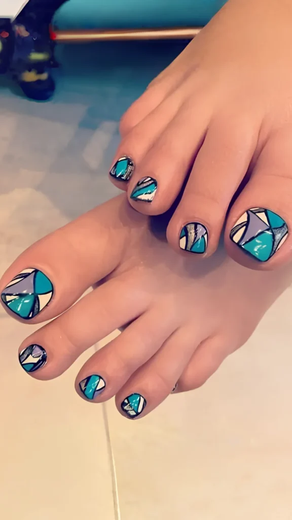 A close-up view of a complete pedicure featuring an intricate geometric mosaic design. The toenails are decorated with an abstract stained-glass pattern using blocks of teal, turquoise, lavender, white, and shimmery silver, all defined by clean black outlines.