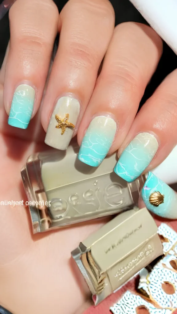 A hand holding a nude-beige bottle of nail polish, showcasing square nails painted with a light blue and sandy-beige beach wave gradient. The nails feature realistic white ripple textures mimicking ocean water, with a small 3D golden starfish charm on the ring finger and a tiny golden seashell charm on the thumb.