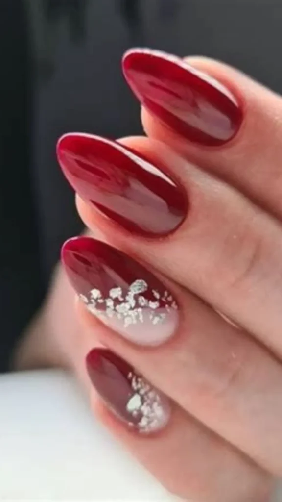 A romantic bridal look featuring glossy, deep cherry-red oval nails. Two accent nails feature a sheer, milky-white base decorated with a gradient cluster of reflective silver foil flakes.