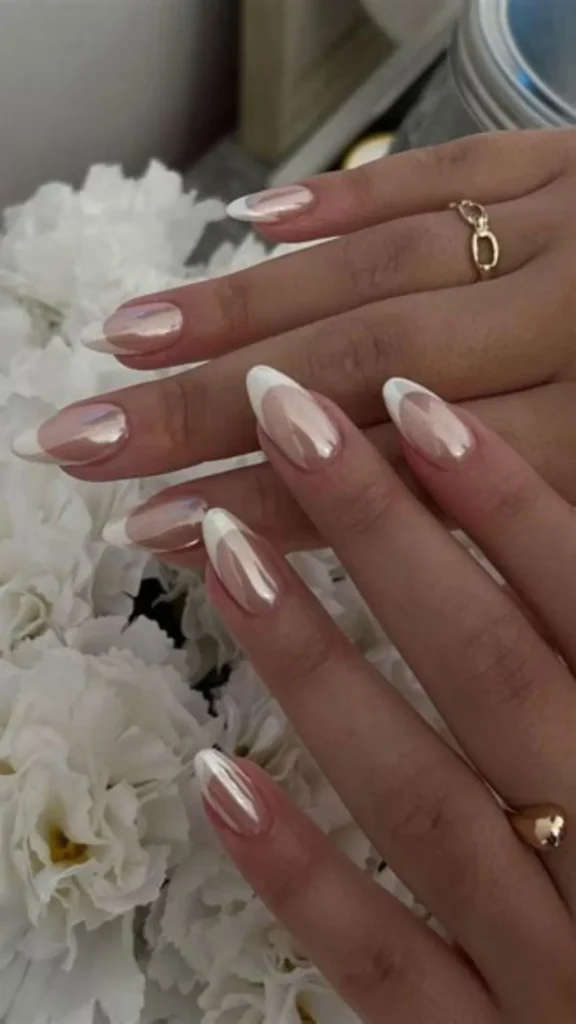 Two hands resting against white flowers displaying an almond-shaped French manicure enhanced with a high-shine, reflective pearlescent glazed chrome finish.
