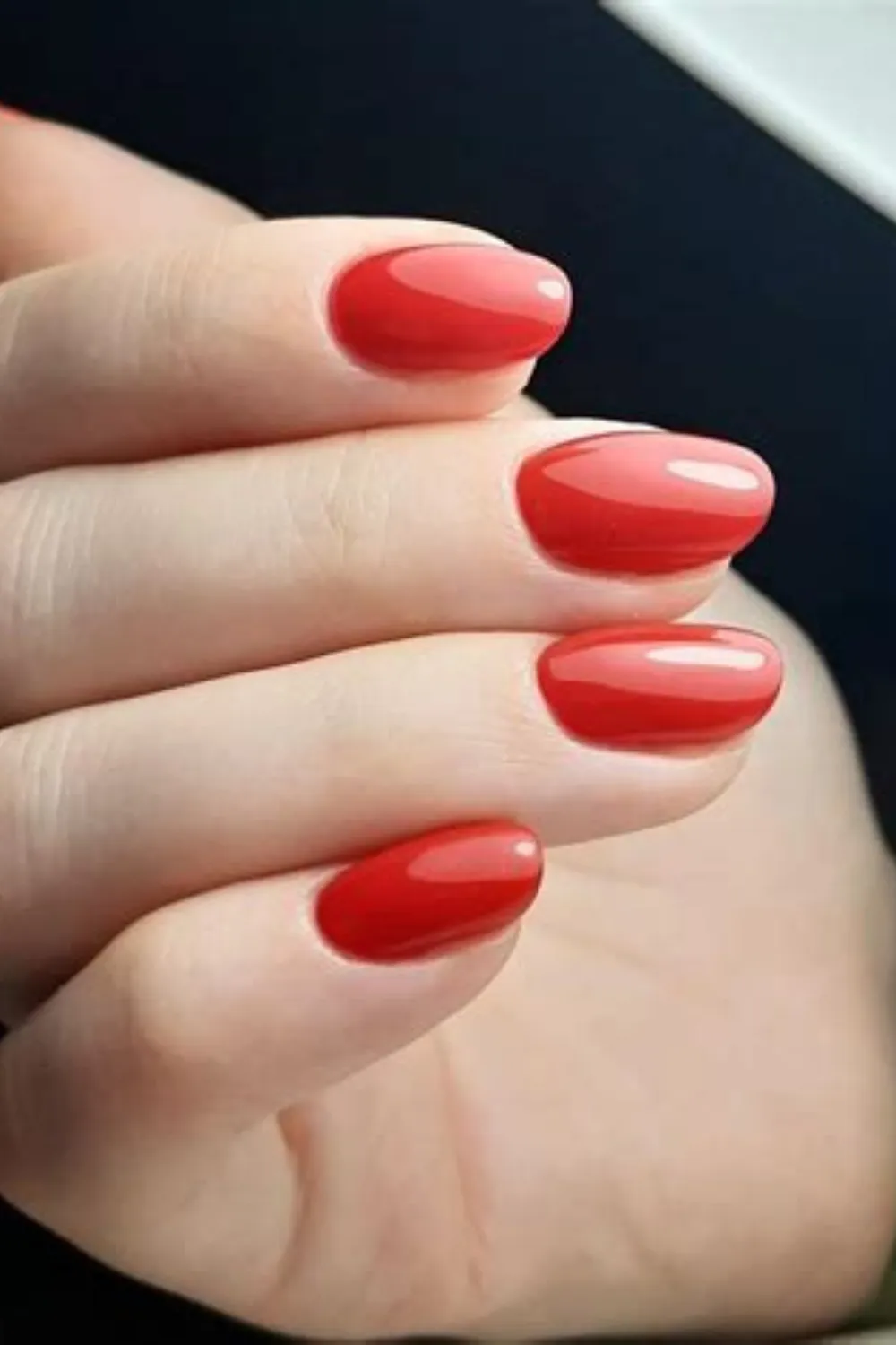 A close-up shot of a hand showcasing a classic, pristine manicure on short, rounded natural nails. The fingernails are painted in a smooth, high-gloss cherry red cream lacquer that delivers an ultra-clean and powerful aesthetic. The pristine top coat reflects long, clean highlights of light, accentuating the well-groomed appearance of the hands.