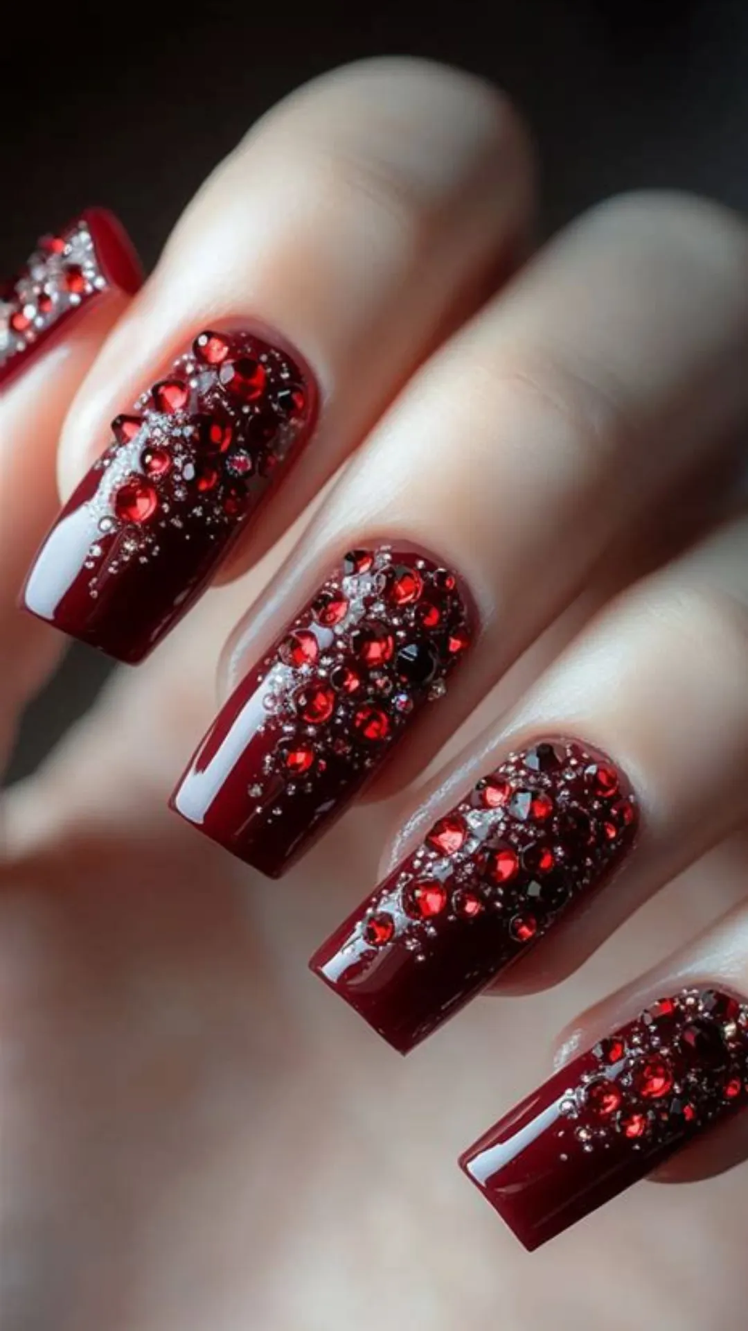 Luxurious holiday nail art featuring long, square-shaped acrylic nails coated in a rich burgundy gel polish and heavily encrusted with glittering red and dark maroon rhinestones.