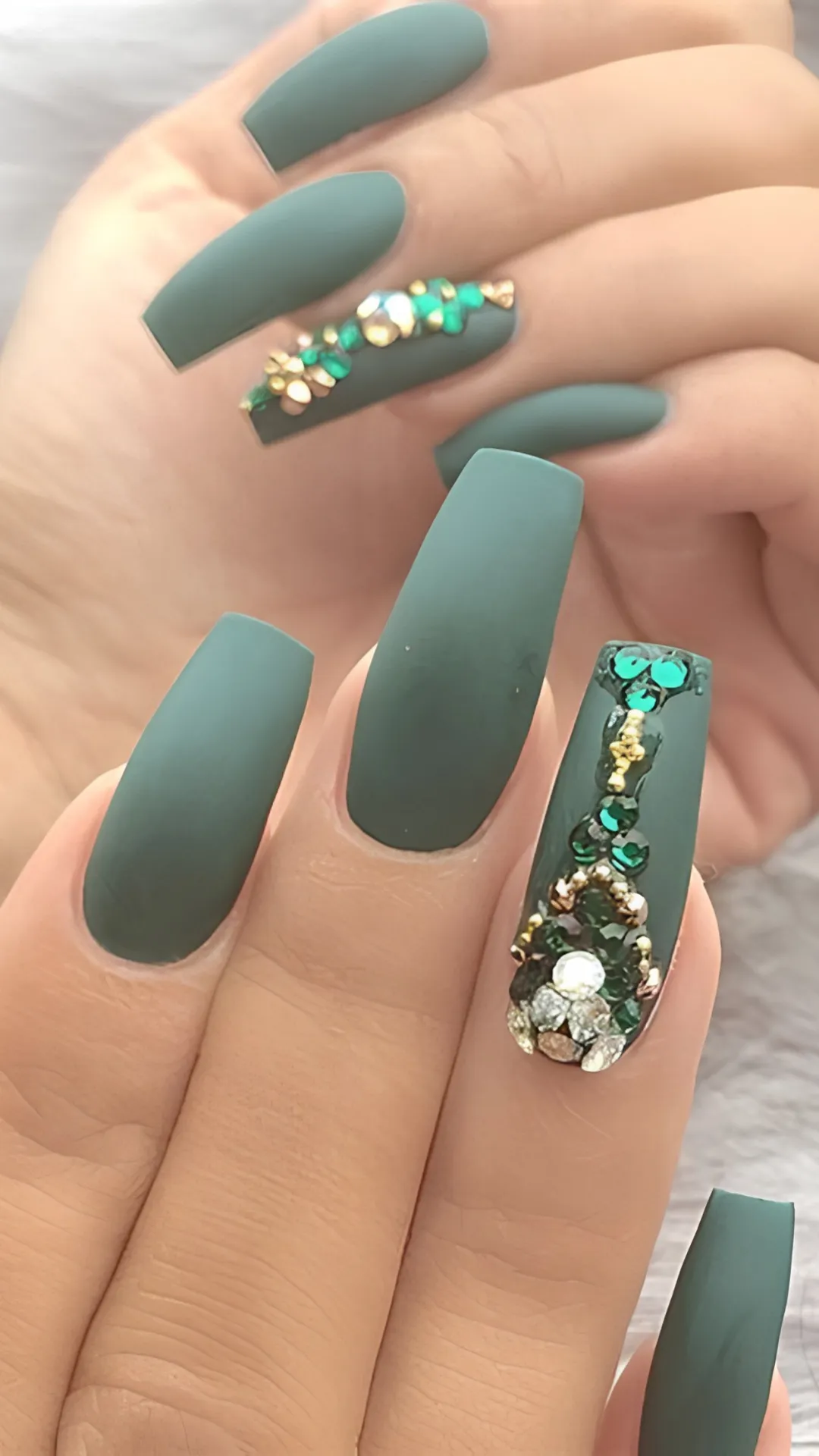 Dramatic long matte green coffin nails heavily embellished with an accent nail encrusted in a vertical design of shimmering emerald, gold, and crystal rhinestones.