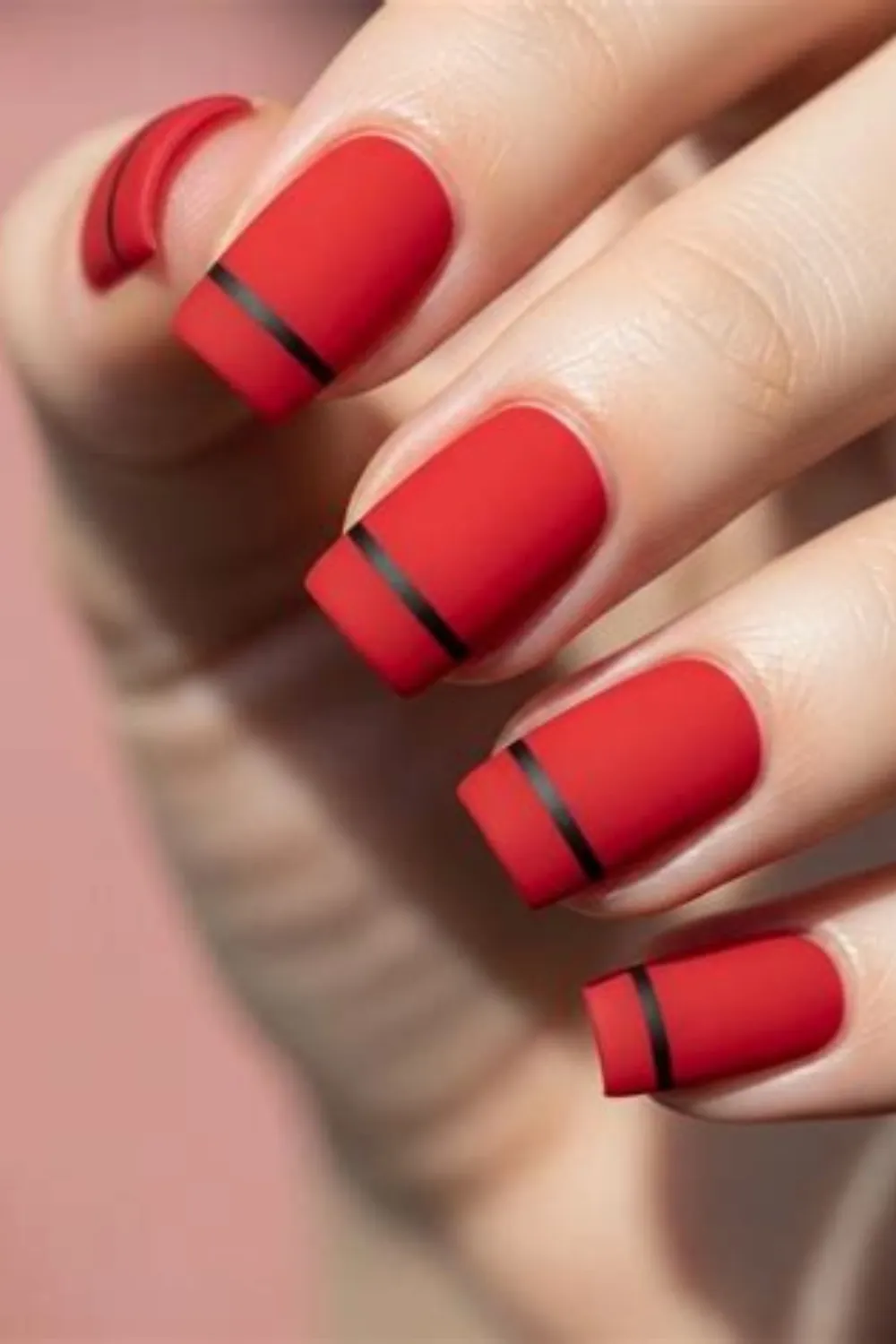 A macro view of a striking minimalist red manicure on short, neatly squared fingernails. The nails are covered in a flawless, full-coverage matte finish in a bright scarlet red hue. A single, crisp graphic line of black polish runs horizontally across each nail bed near the tips, creating a modern, structured, and contemporary look.