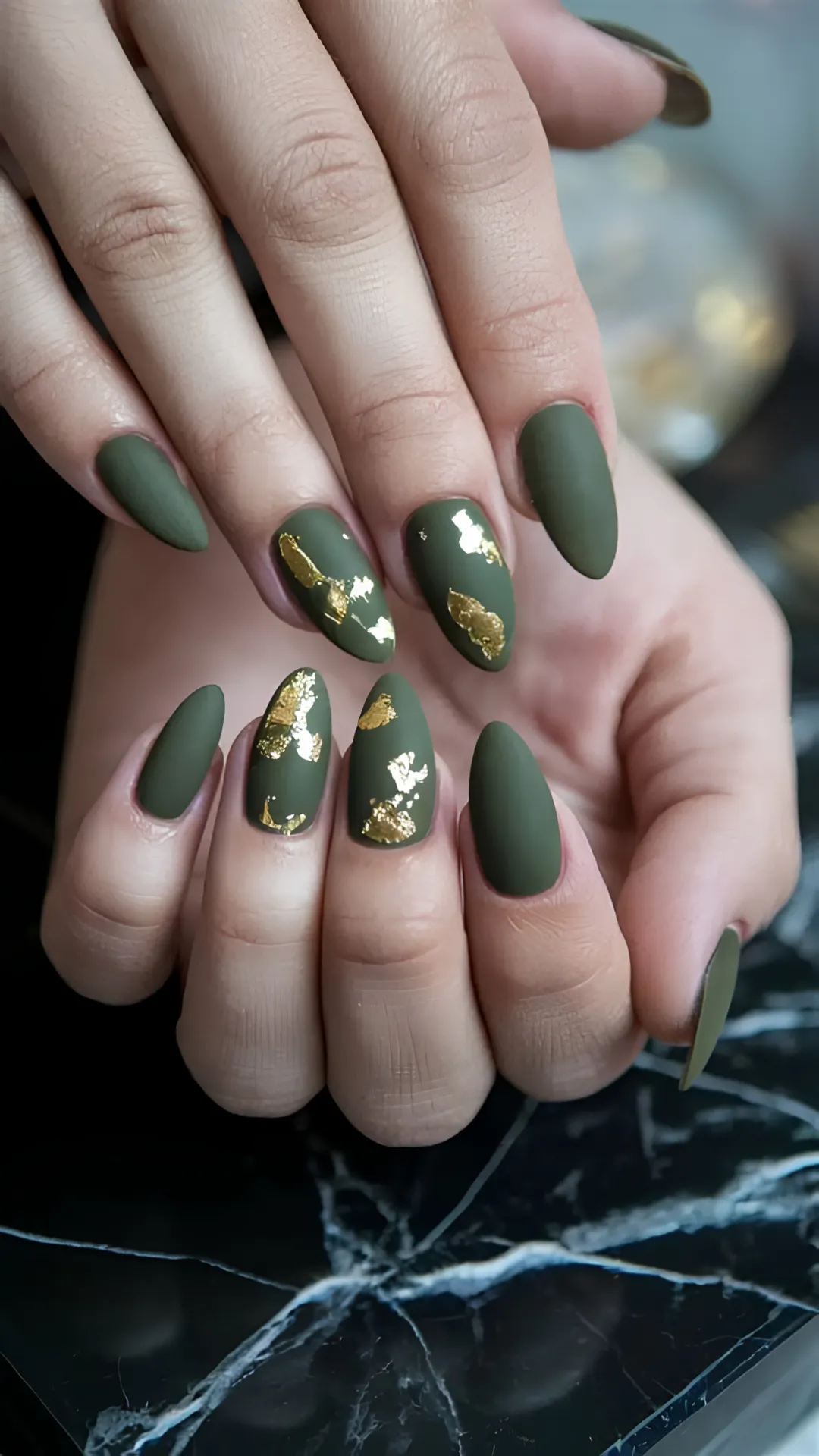 Elegant almond-shaped nails coated in an earthy matte olive green polish, accented with organic splashes of metallic gold foil flakes.