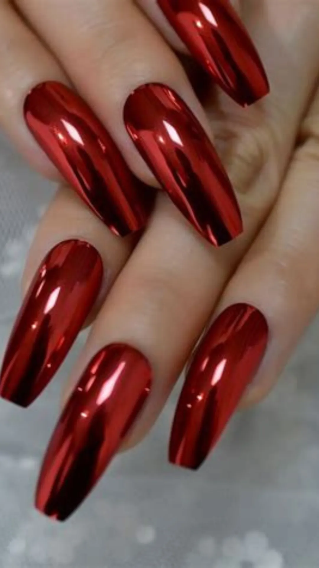 An extreme close-up view of a high-impact, futuristic manicure on long, square-shaped nails. The nails are covered in a flawless, highly reflective metallic chrome powder in a striking candy-apple or cherry red shade. The liquid-like, mirrored surface gleams intensely, giving the nails a bold, edgy, and unapologetic appearance.