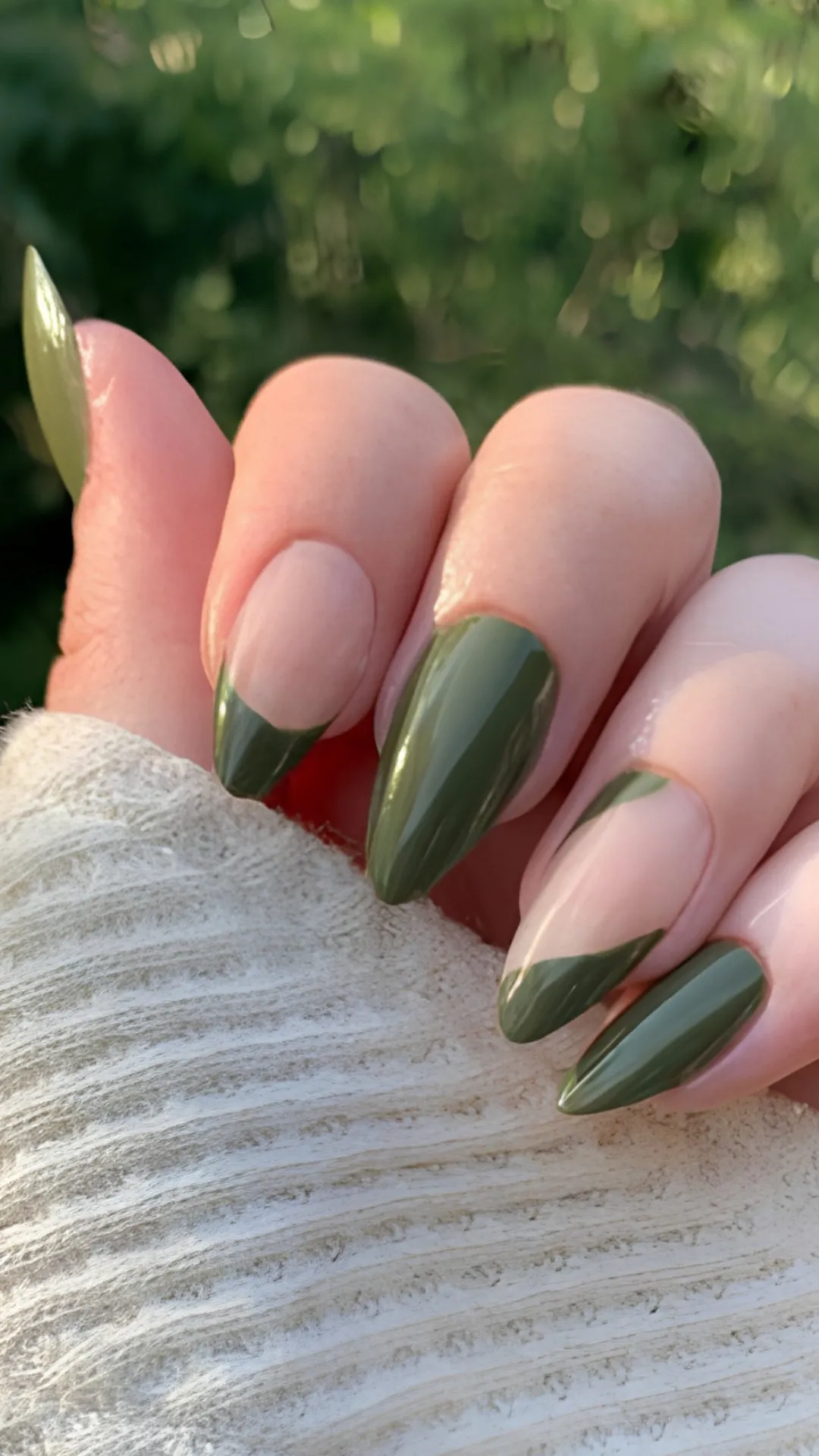 Trendy negative-space nail art on glossy almond nails, featuring a clear natural base with deep olive green wavy, abstract French tips.