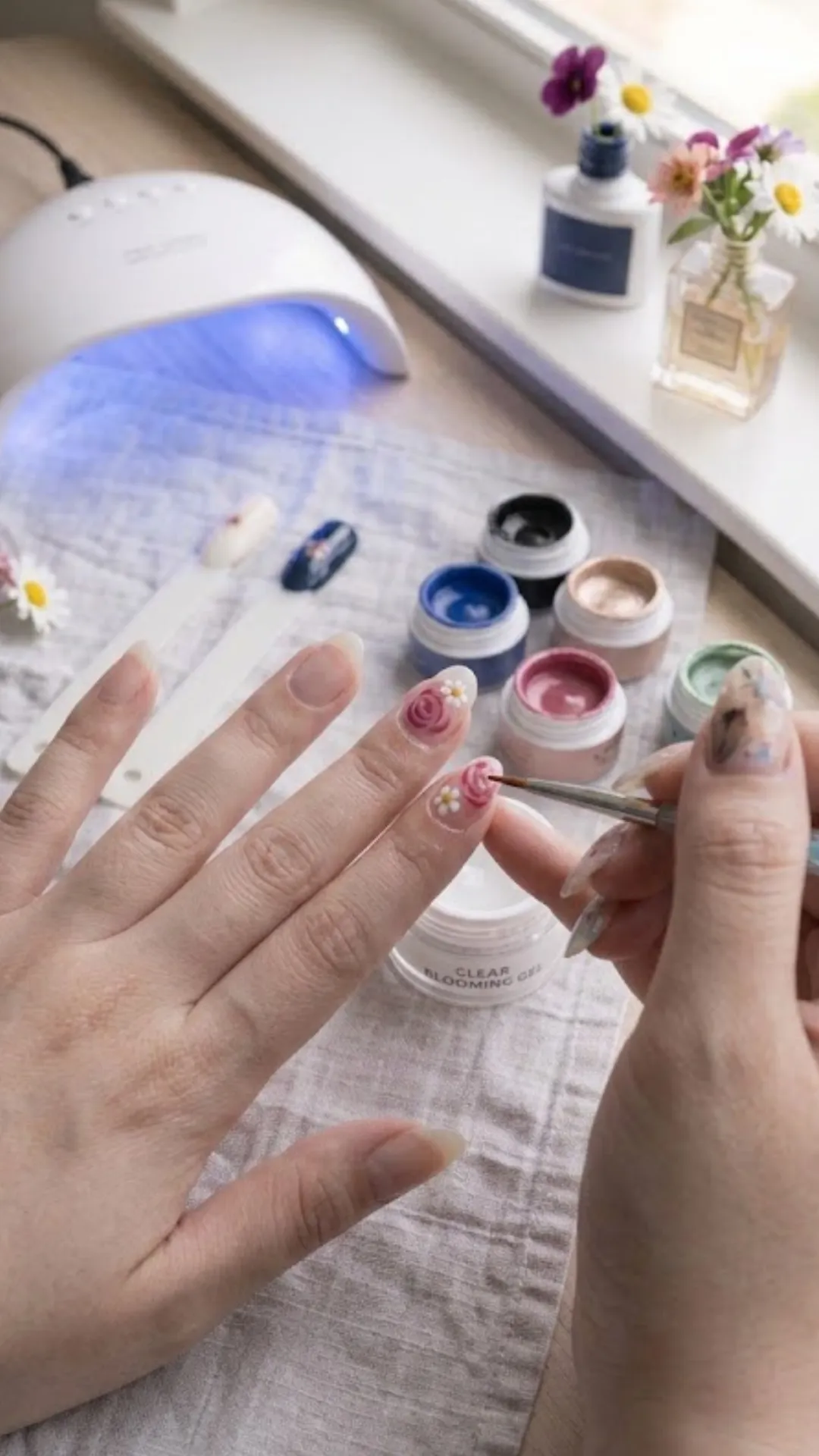 The next step in the blooming gel nail tutorial, showing how the blue dots have spread out into soft, translucent watercolor flower shapes, with additional white and pink floral details being added to adjacent nails.