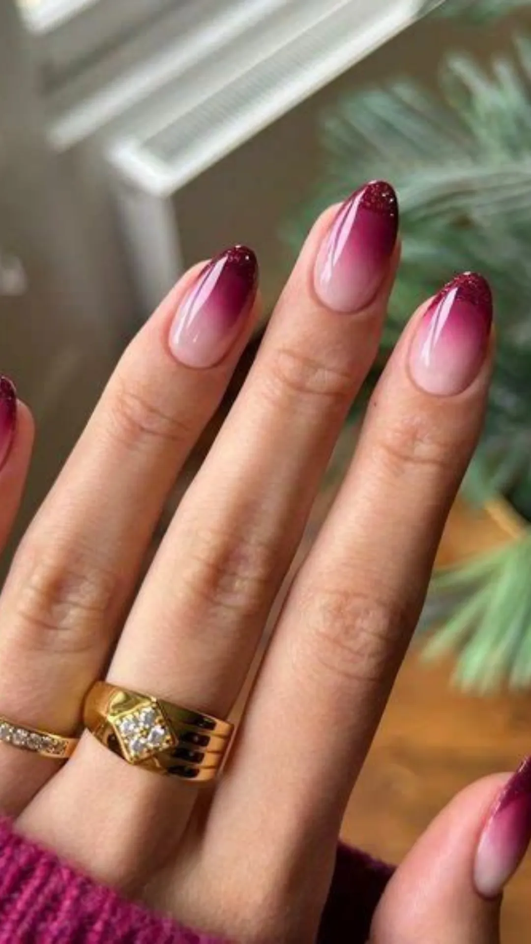 A smooth, chic ombre manicure displaying almond nails with a soft gradient that blends from a neutral nude base into deep, glittery burgundy tips.