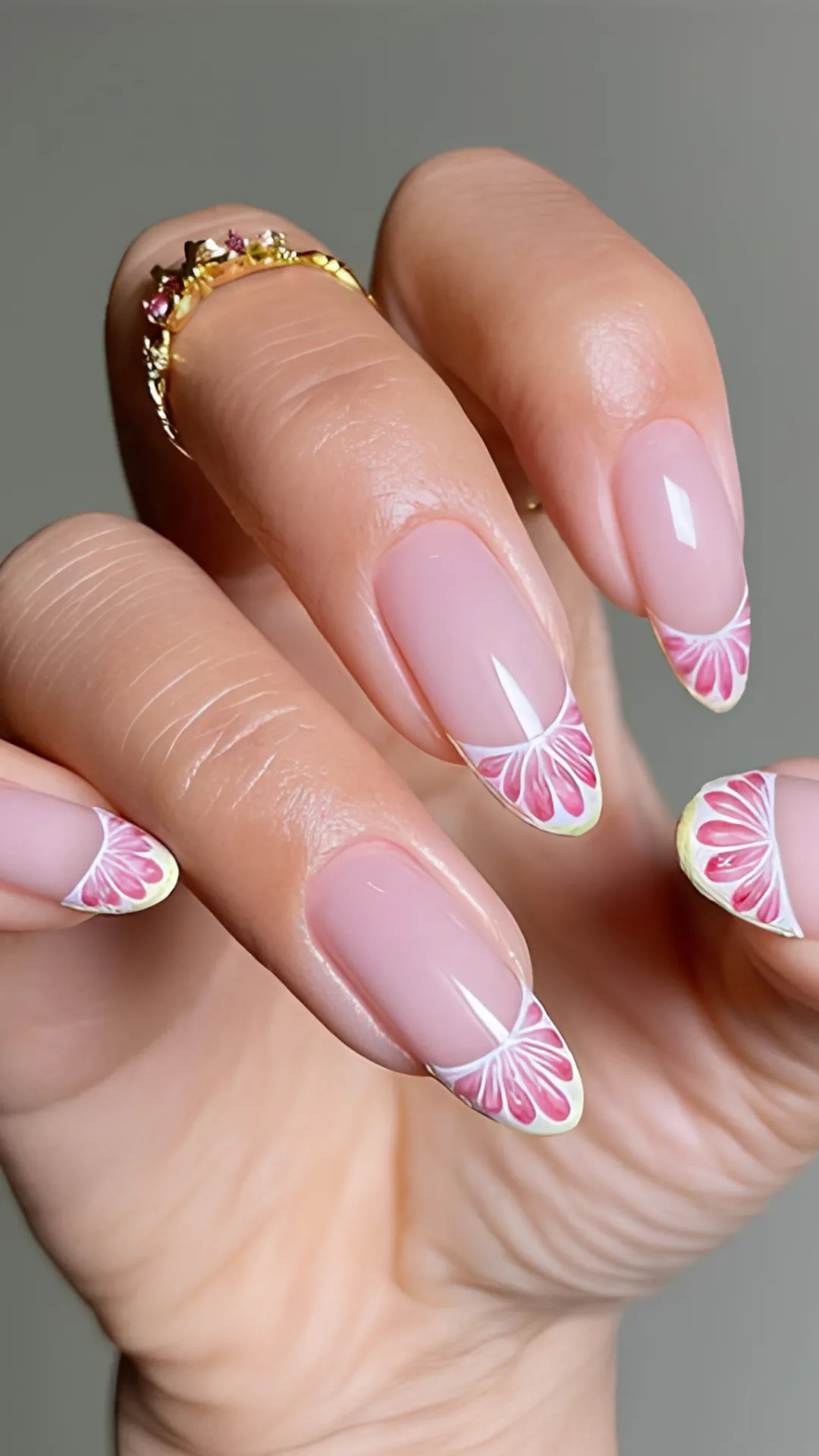 An elegant close-up of a hand displaying a delicate floral twist on the classic French manicure. The long, oval-shaped nails feature a clean, glossy sheer pink base coat. Instead of traditional white tips, the nail edges are meticulously hand-painted with detailed pink flower petals outlined in white, mimicking the look of blooming chrysanthemums or dahlias at the tips.