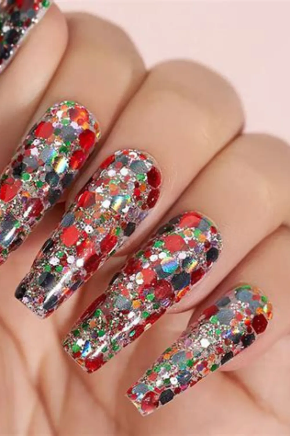 A close-up shot of a hand showcasing an ultra-sparkly festive manicure on long coffin nails. Every single nail bed is densely packed with multi-sized, chunky hexagonal glitter flakes in reflective silver, ruby red, emerald green, and holographic colors, creating an intense, blinding sparkle from every angle under the light.
