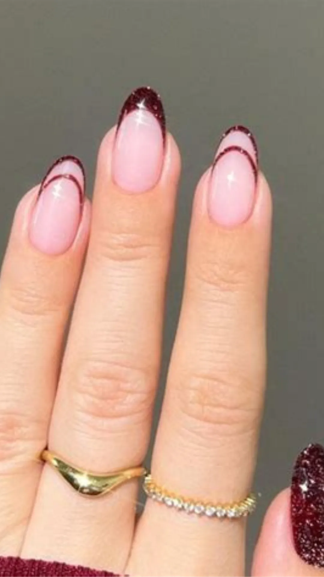 Modern and minimalist French manicure variation featuring oval nails with a sheer pink base, detailed with shimmering burgundy glitter tips and thin double arch lines.