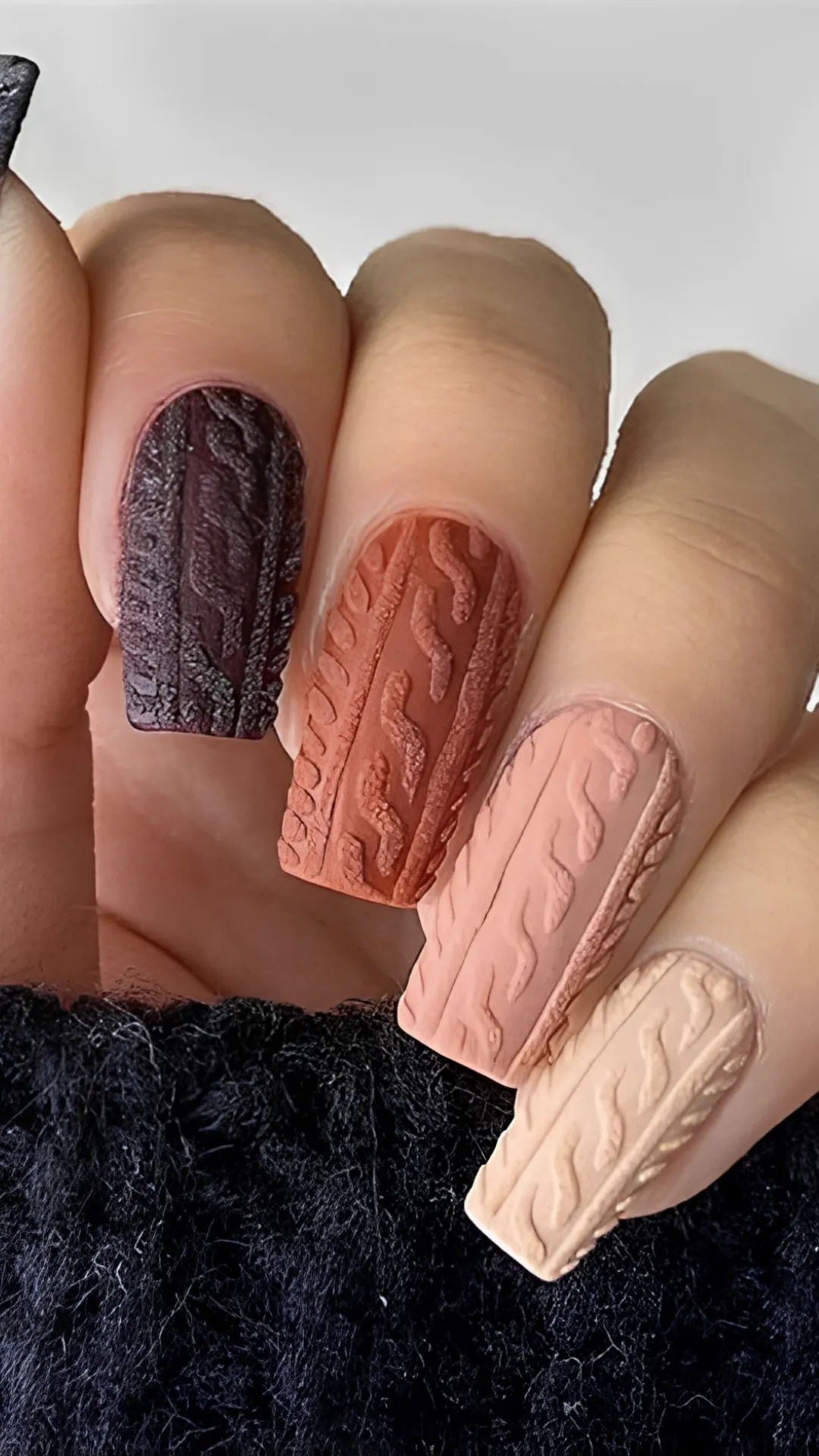 A sophisticated fall look featuring a gradient of square nails textured with 3D embossed cable-knit sweater patterns in dark plum, terracotta orange, mauve pink, and cream.