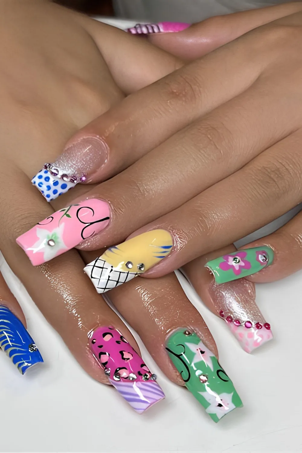 A detailed composite photo displaying maximalist Y2K mix-and-match duck or flare nails. The extra-long square nails feature an array of nostalgia-packed patterns on each finger, including pink leopard print, blue polka dots, yellow plaid, green Hawaiian flowers, and silver glitter bases lined with hot pink rhinestone gems along the cuticles.