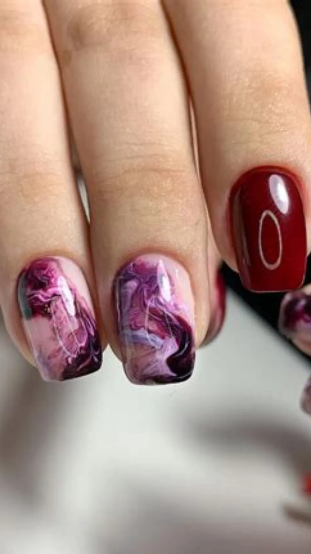 Sophisticated short square manicure featuring a mix of solid, high-gloss burgundy nails and artistic watercolor fluid marble accent nails in shades of purple, pink, and deep wine.